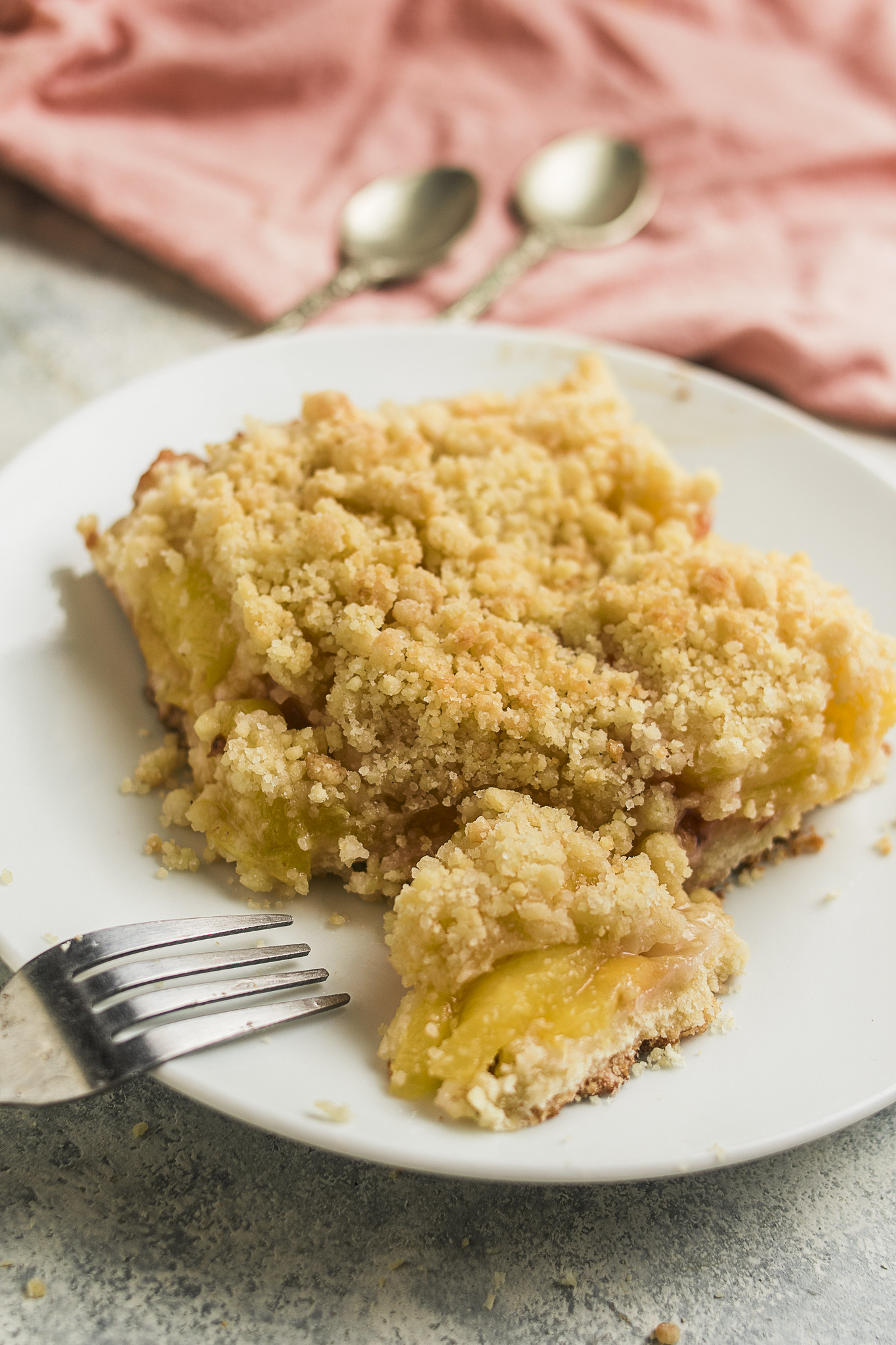 Close-up of a slice of sbriciolata di pesche on a white plate, showing the crumbly topping, soft peach filling and buttery base.